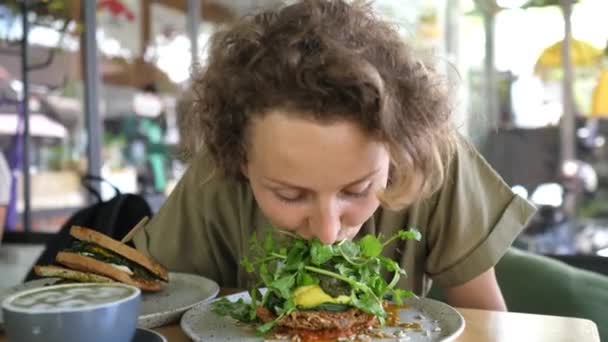 Fröhlich hungernde junge Frau isst ihren veganen Toast ohne Hände — Stockvideo