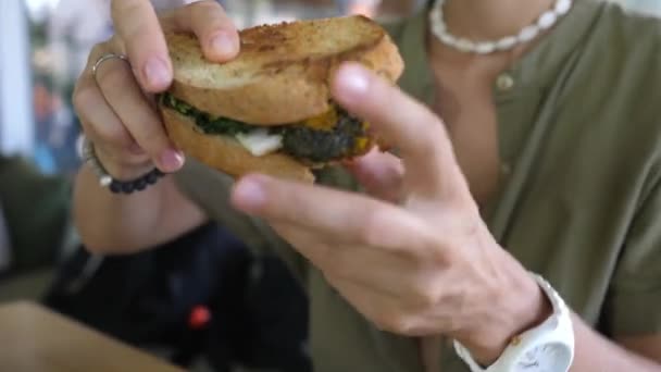 Tânăra femeie caucaziană iubitoare de mâncare ia un sandwich vegan organic sănătos, îl mușcă cu poftă de mâncare și îl privește cu apreciere — Videoclip de stoc