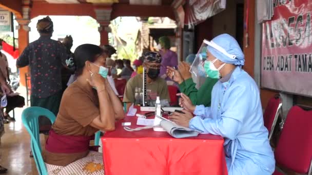 Zewnętrzny ośrodek szczepień przeciw wirusowi covid-19. Pracownik medyczny przesłuchuje kobietę przed zabiegiem. Bali-Indonezja-marzec 2021 r. — Wideo stockowe
