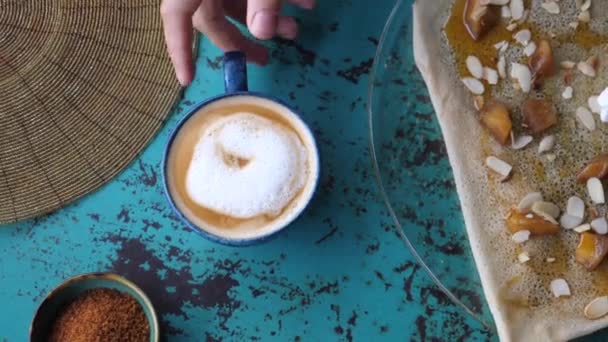 Ręce podnoszące kubek roślinnej kawy latte od niebieskiego stołu — Wideo stockowe