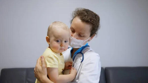 Nurse in face cover cuddling sad baby in arms to calm down and ease stress. Frontline healthcare workers help families during coronavirus threat