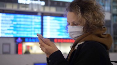 Coronavirüs salgını sırasında toplu taşıma sektörü. Yüzü maskeli bir kadın, telefon kartı ile panoya bakıyor.