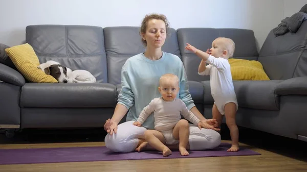Auto-cuidado e tempo pessoal de vida pais ocupados. Mãe solteira tenta meditar sobre tapete de ioga em casa com duas crianças ativas em torno de distraí-la — Fotografia de Stock