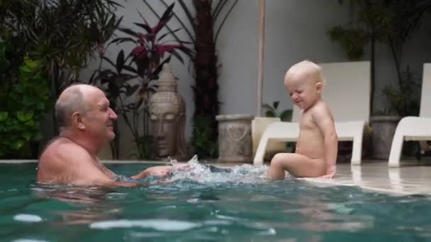 Bambino caucasico spruzza acqua nella piscina a giocare con il nonno. La vita in villa con la famiglia amorevole — Video Stock