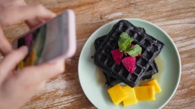 Ellerin akıllı telefonlu Belçika wafflelarının fotoğrafını çekerken üst görünümü. 