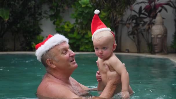 Glücklicher Großvater und Baby tragen Weihnachtsmützen im Schwimmbad. Urlaub und Urlaubskonzept. — Stockvideo
