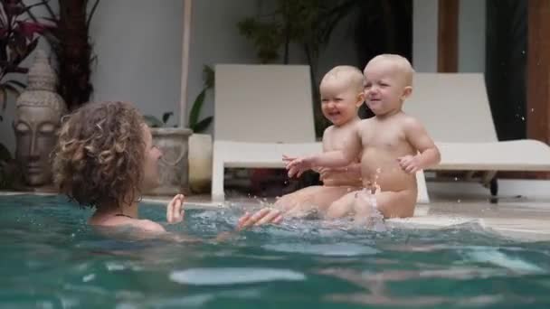 Feliz paternidade solteira. Jovem mãe brincando com seus bebês gêmeos na piscina privada — Vídeo de Stock