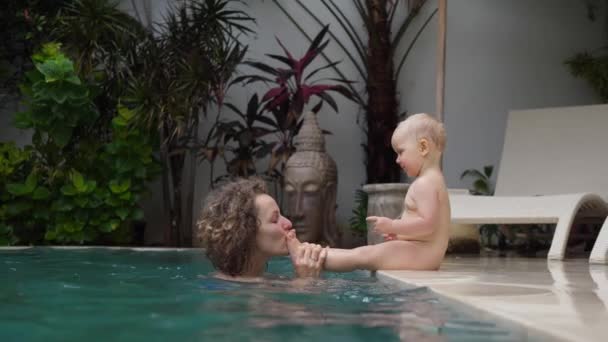 Young Caucasian mother plays with her baby toddler at the private swimming pool. Mother child bond — Stock Video