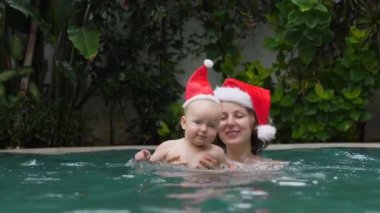 Mutlu Anne ve Bebek Yüzme havuzunda Noel Baba Şapkası Giyiyor.