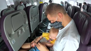 Baba, bebek kızıyla uçuyor. Yüzü maskeli, uçakla seyahat ediyor. Covid-19 pandemik konsepti sırasında çocuklarla normal seyahat ediyor.. 