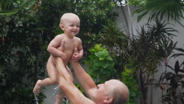 Isoisä leikkii uima-altaassa lapsenlapsensa kanssa. Onnellinen perhe lomalla — kuvapankkivideo