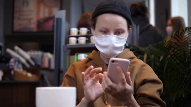 Företag på offentliga platser mitt i covid-19 utbrott. Kvinnan i caféet tar bort ansiktsmask för att dricka kaffe med äppelpaj medan du läser de senaste nyheterna online. — Stockvideo