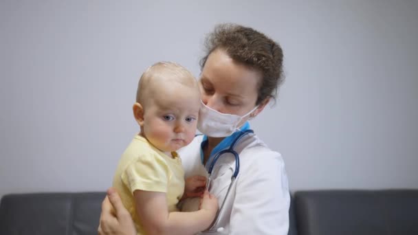 Sköterska i ansiktet täcka krama ledsen baby i armar för att lugna ner och lindra stress. Frontline sjukvårdspersonal hjälpa familjer under coronavirus hot — Stockvideo