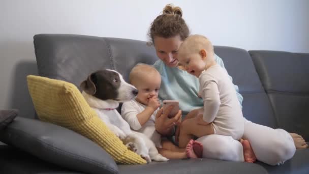 Jovem mãe e bebê gêmeos jogando com um telefone inteligente em casa. — Vídeo de Stock