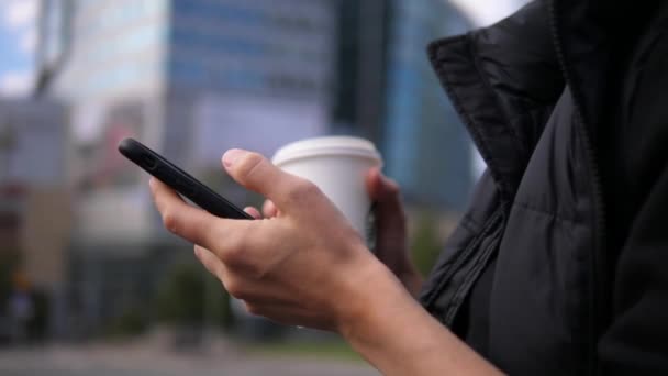 Close up de mãos femininas com takeaway bebida quente usando telefone celular na rua da cidade. Vida digital moderna em movimento — Vídeo de Stock