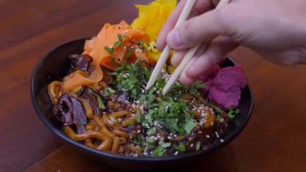 Veganistisch Aziatisch blog voor trendy recepten. Close up van de hand mengen kleurrijke ramen udon op zwarte plaat met stokjes — Stockvideo