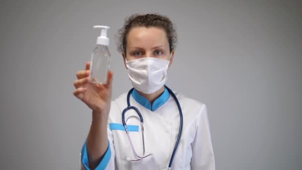 Caucásico médico femenino con mascarilla muestra gel de mano desinfectante a la cámara — Vídeos de Stock