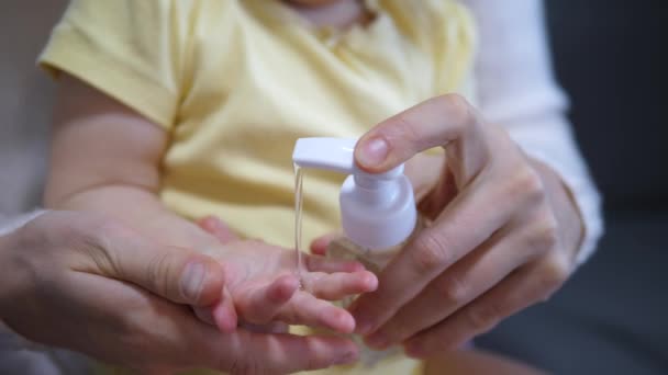 Primer plano de la mano de las personas adultas poniendo gel antibacteriano desinfectante en la mano de los bebés pequeños — Vídeos de Stock