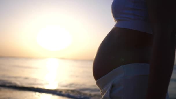 Close-up van de jonge zwangere moeder wandelen bij zonsondergang op het strand. Zonsondergang wandeling op zee badplaats — Stockvideo