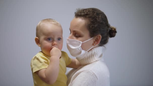 Vida familiar durante la crisis del coronavirus. El niño curioso quita la máscara de la cara de las madres para besar — Vídeo de stock