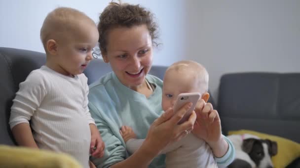 Lycklig mamma spelar roliga onlinespel med nyfikna bebissyskon på telefon. Familj kvalitetstid med hemaktiviteter tillsammans — Stockvideo