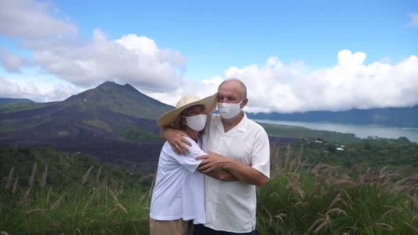 Portret van koppels van middelbare leeftijd met gezichtsmaskers die knuffelen voor de bergen en de oceaan. Reizen tijdens de covid-19 pandemie — Stockvideo