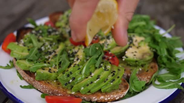 Sluiten van de hand besprenkelen citroen over groene salade op toast met avocado smash. Gezond plantaardig dieet voor een lange levensduur — Stockvideo