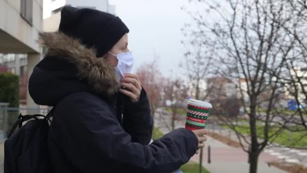 Žena na ulici s maskou a s kávou před sebou během koronaviru. WARSAW, POLSKO, 12 DEC, 2020. — Stock video