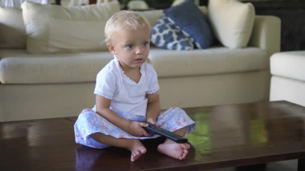 Una niña caucásica sentada en el suelo viendo la televisión con control remoto — Vídeo de stock