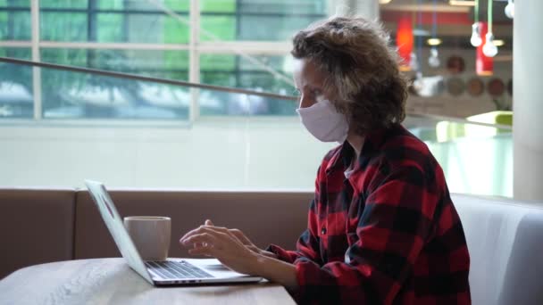 Цифрова культура кочівників під час спалаху коронавірусу. Блогер жінка в масці для обличчя, що працює на комп'ютері в громадському коворкінгу — стокове відео