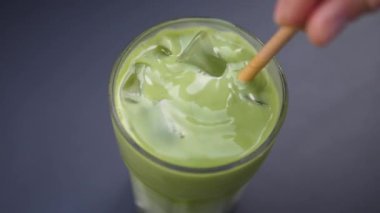 Buzlu kibrit sütlü kahveyle uzun bardaktaki tahta sopayı karıştıran el manzarası. Soğuk içeceklerdeki yaz trendi