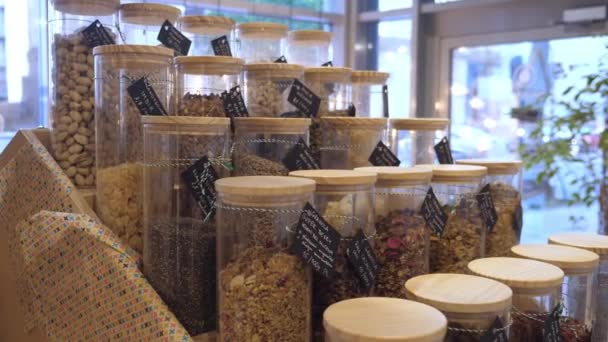 Granola, kacang-kacangan, biji-bijian, sereal, buah-buahan kering dalam toples kaca tinggi untuk dijual. Paket toko bebas sebagai solusi berkelanjutan bagi konsumen yang sadar lingkungan — Stok Video