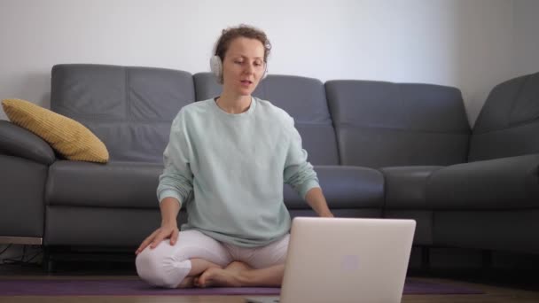 Молода жінка навчається вдома використовуючи ноутбук робить йогу онлайн курс . — стокове відео