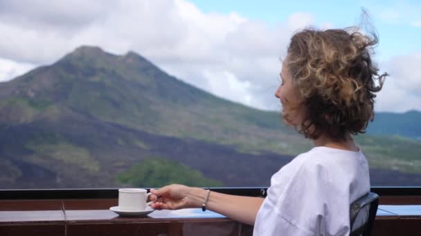 女性のバルコニーに座って山の景色を楽しむ熱い飲み物を飲むのバックビュー — ストック動画