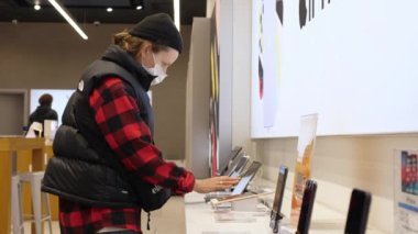 Coronavirus 'a karşı koruyucu yüz maskesi takan genç bir kadın salgın sırasında alışveriş yaparken Apple Store' da yeni akıllı telefon seçiyor. Varşova, Polonya, 26 Kasım 2020.