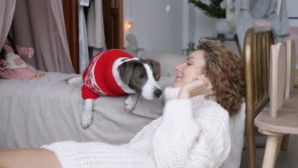 Mujer joven juega con el perro esperando a que los invitados lleguen para la cena en casa de Año Nuevo. Felices mascotas y dueños celebrando vacaciones de invierno juntos — Vídeos de Stock