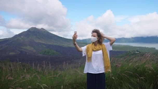 Mulher caucasiana usando máscara facial tendo videochamada nas montanhas, mostrando a paisagem. Permanecer conectado durante o vírus corona — Vídeo de Stock