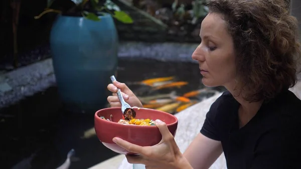 Kaukasiska flicka äter sin friska vegan megan i restaurangen med en damm med koi karpar i den. REstaurant med utsiktskonceptet — Stockfoto