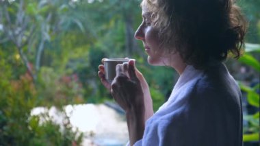 Sabah kahvesinin kokusunu alan bir kadın. Dışarıda durmuş, Bali doğasının tadını çıkarıyor. 