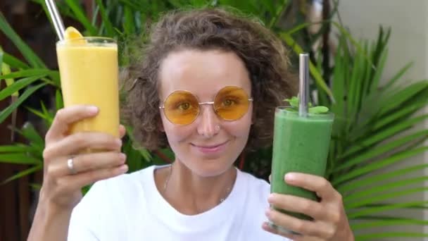 Běloška ukazuje kameře zelené a žluté smoothies se snaží rozhodnout, který z nich mít — Stock video