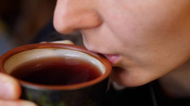 Kadın siyah çaya üfledi ve seramik çay fincanından içti. Çay sanatı.