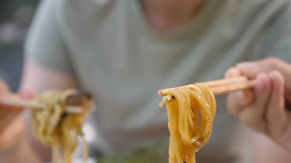 Trendy greasy Asian street food. Close up of noodles from ramen soups hanging on the chopsticks.