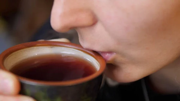 Kobieta dmucha na czarną herbatę i podpuszcza ją z ceramicznej filiżanki herbaty. Sztuka koncepcji herbaty — Zdjęcie stockowe