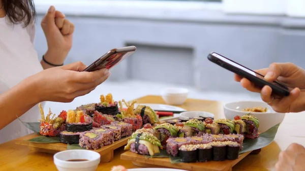 Två personer tar bilder på sina färgglada veganska sushi set med smartphones under lunchen. Friska vegan livsstil koncept — Stockfoto