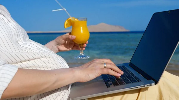 Беременная женщина работает с ноутбуком на пляже у моря. — стоковое фото