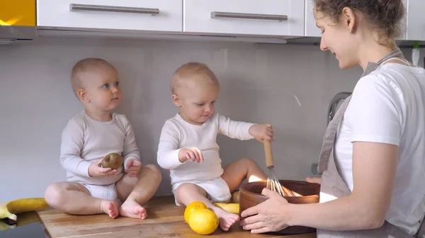 Mãe jovem e bebês gêmeos fofos comem bananas orgânicas na cozinha. Nutrição equilibrada saudável para crianças. — Fotografia de Stock