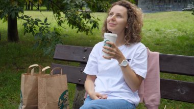 Parkta oturan beyaz kız Starbucks içkisinin tadını çıkarıyor. Varşova-Polonya-2020