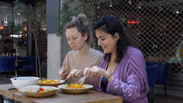 Meninas loiras e morenas desfrutando de jantar juntos. Amigos conversando sobre refeição saudável e colorida no restaurante estilo loft. — Fotografia de Stock