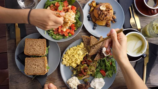 Ovanifrån av händer äter hälsosam ekologisk vegan frukost full engelska, pastasallad och vegan pannkakor serveras på träbord — Stockfoto