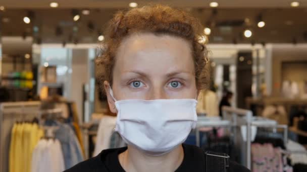 Deuxième vague de propagation du virus corona concept. Portrait d'une jeune femme portant un masque de protection posant devant une caméra dans un magasin de vêtements pendant une pandémie de covidé-19. — Video